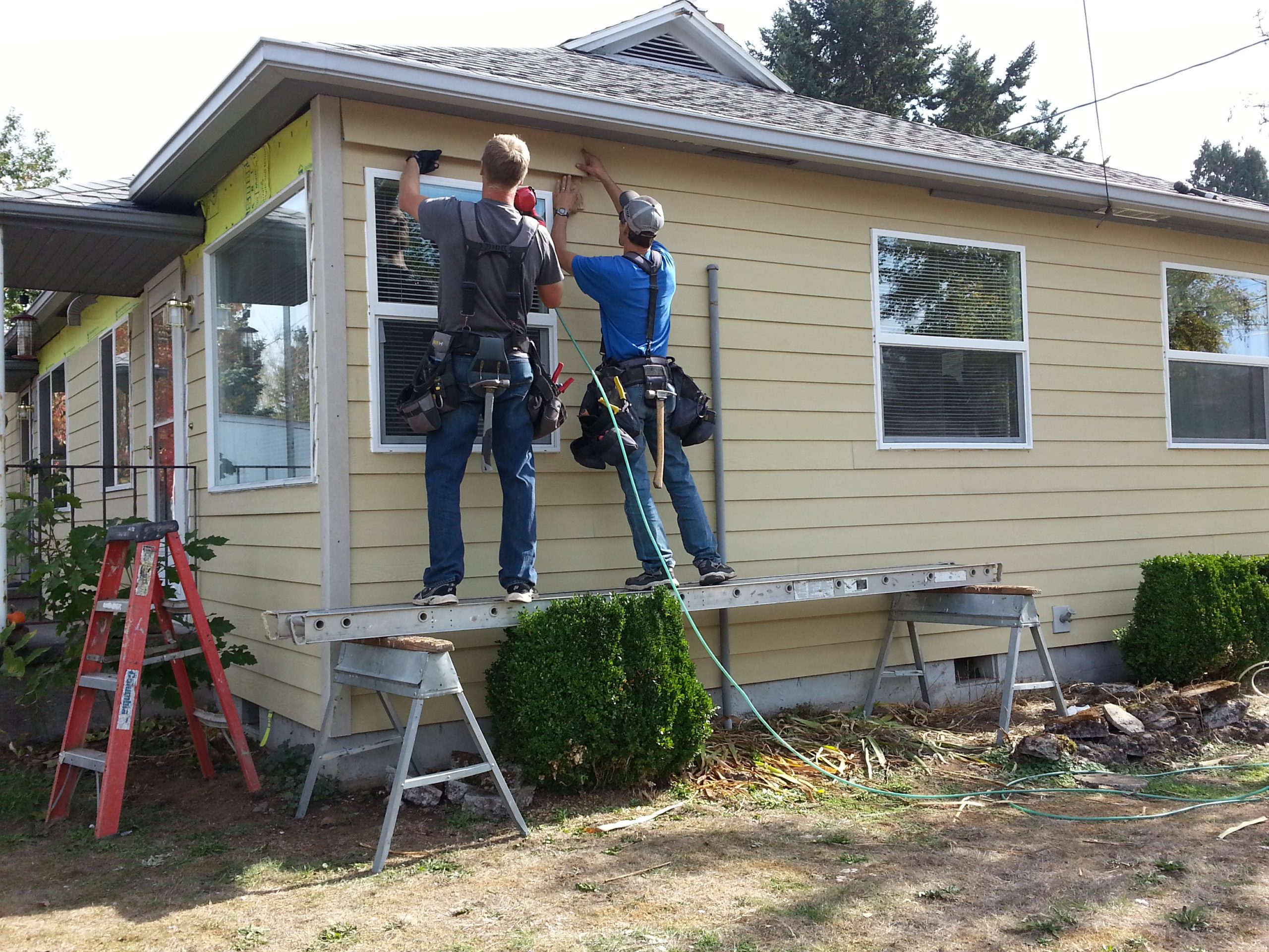 Workers putting siding on house around new vinyl windows